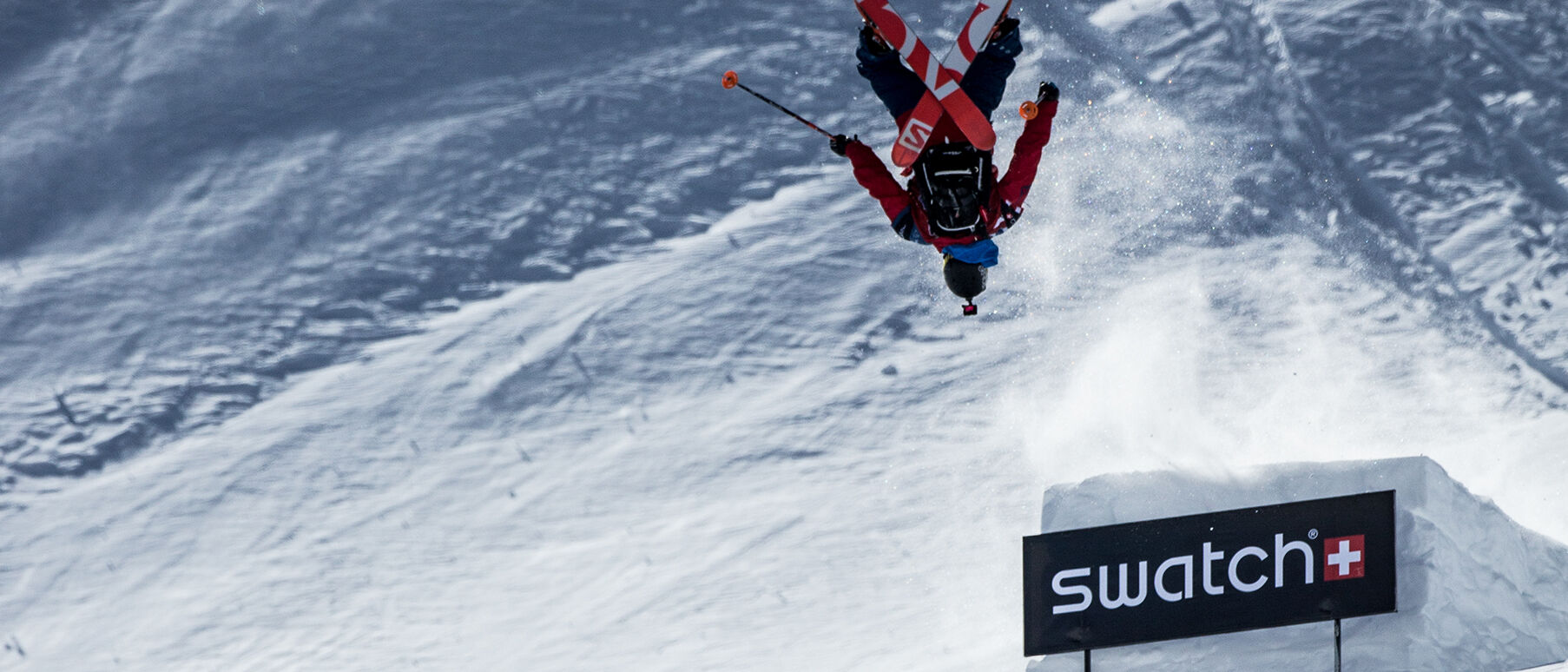 A Swatch Proteam professional skier performing a backflip from a snow ramp 