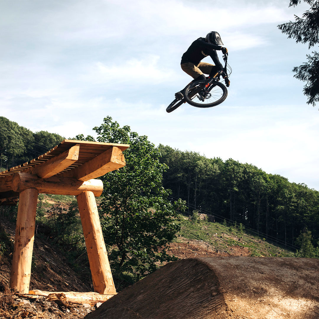 A mountain biker jumps off a wooden ramp with his bike